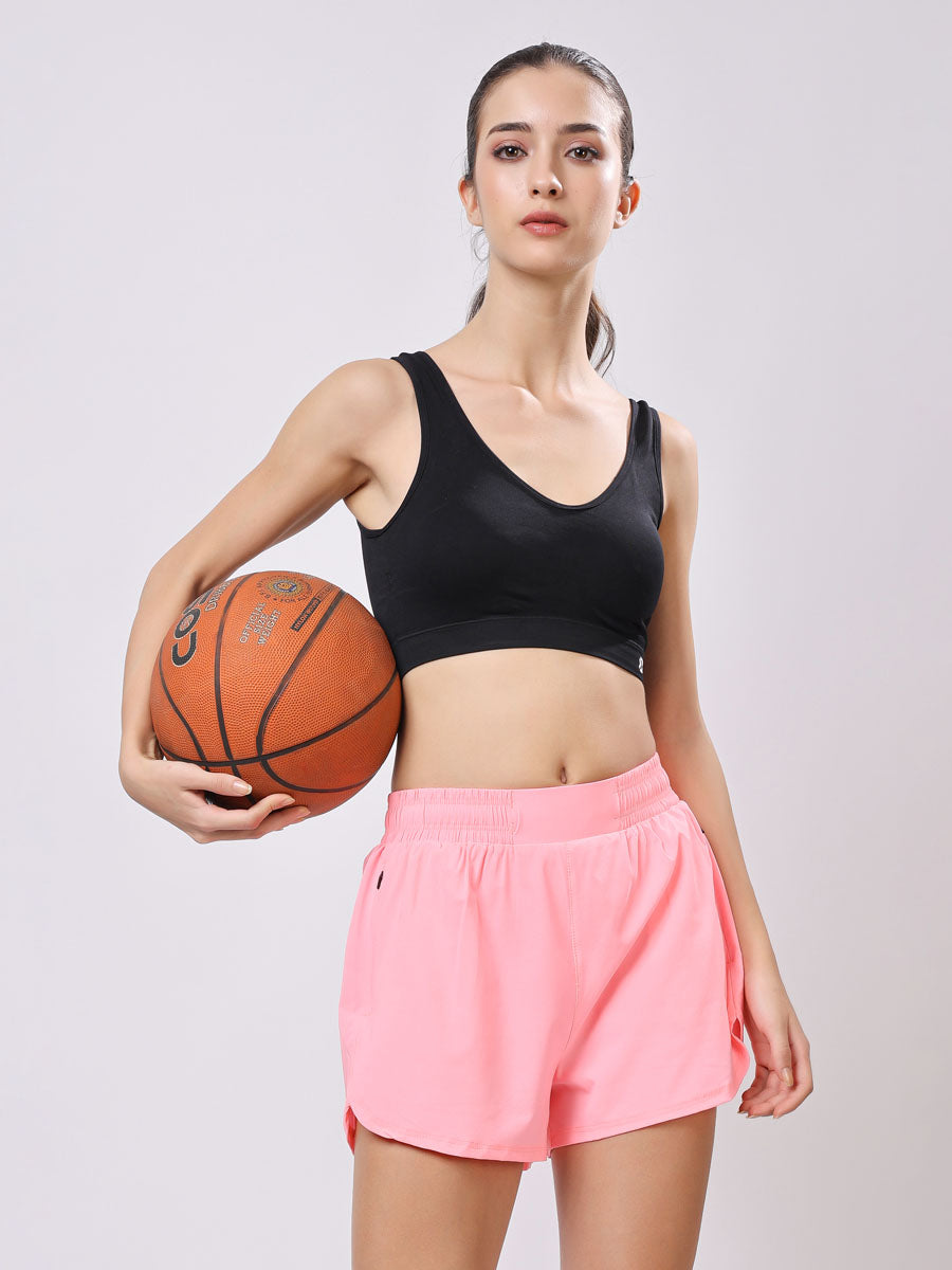 Woman holding a basketball wearing a black sports bra and pink shorts on a light gray background
